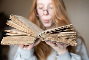 Młoda kobieta zdmuchuje kurz ze starej książki.