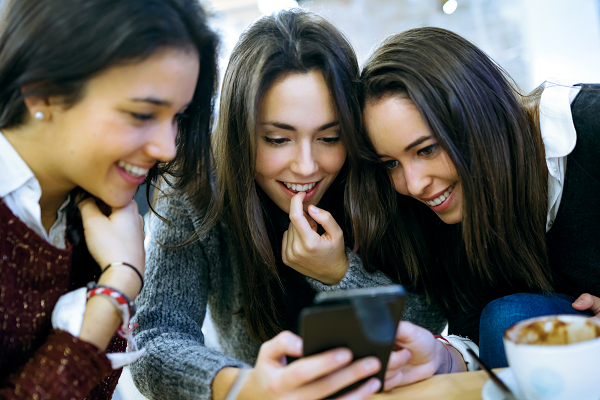 Trzy młode kobiety sprawdzają na telefonie jak szybciej uczyć się języków obcych.