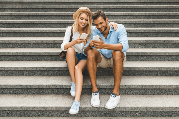 Para młodych ludzi w letnich ubraniach korzysta ze swoich smartfonów. Oboje siedzą na schodach.