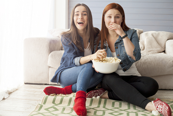 Dwie kobiety jedzą popcorn i oglądają wspólnie telewizję.