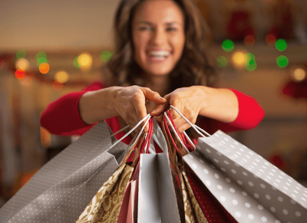 Kobieta podczas świątecznych zakupów trzyma przed sobą kilka toreb prezentowych.